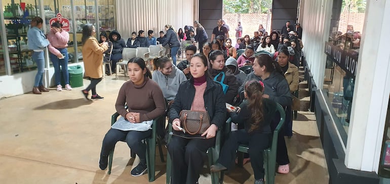 Dos mujeres en primera fila, una de chaqueta negra y otra mirando al frente, rodeadas de personas en un ambiente de reunión.