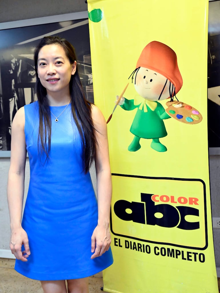 Mujer con vestido azul y cabello largo frente a un banner de ABC Color, mostrando una expresión amigable.