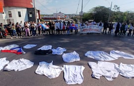 Grupo de médicos con batas blancas y carteles en protesta, rodeados de vehículos y un ambiente urbano.