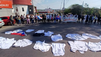 Grupo de médicos con batas blancas y carteles en protesta, rodeados de vehículos y un ambiente urbano.