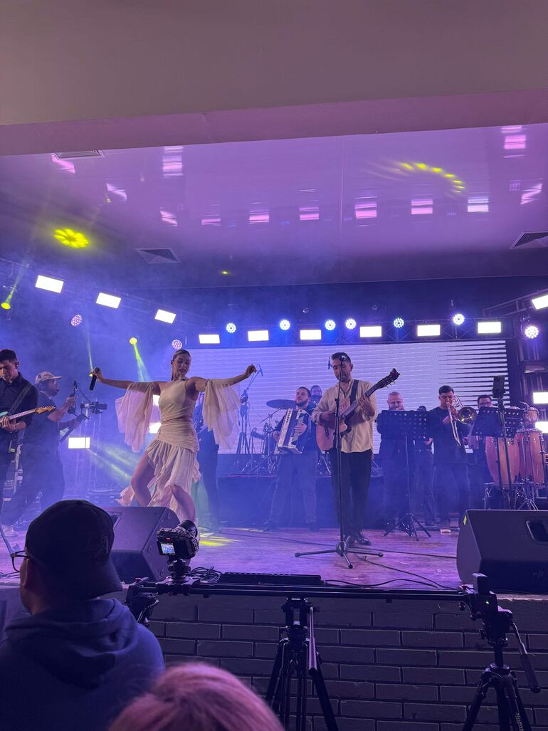 Sol Codas en vestido blanco canta con micrófono, mientras Marcelo Gabriel toca la guitarra rodeados de músicos y luces de colores.