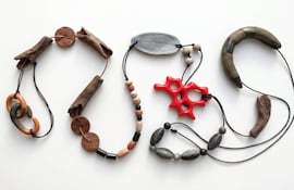 Collares de madera, cerámica y cuentas de colores sobre fondo blanco, mostrando formas abstractas y naturales.