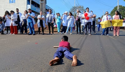 Médicos con batas blancas sosteniendo carteles amarillos, mientras un niño en el suelo sostiene un cilindro de cartón.