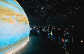 Persona de pie explicando sobre Júpiter a un grupo atento en un entorno del museo, bajo luces que simulan estrellas.