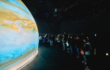 Persona de pie explicando sobre Júpiter a un grupo atento en un entorno del museo, bajo luces que simulan estrellas.