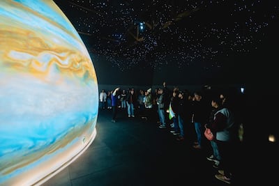 Persona de pie explicando sobre Júpiter a un grupo atento en un entorno del museo, bajo luces que simulan estrellas.