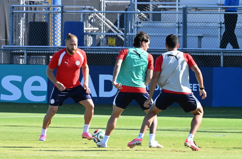 Isidro Pitta, con camiseta roja, junto a dos jugadores en campo de césped, concentrados en ejercicios de fútbol.