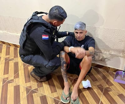 Hombre en chaleco de seguridad agachado cerca de otro hombre canoso sentado, en un ambiente de pared manchada.