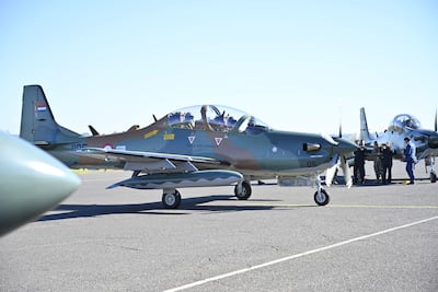 Dos pilotos en la cabina del Super Tucano mientras un grupo de personas en uniforme y civil discute alrededor en un día soleado.