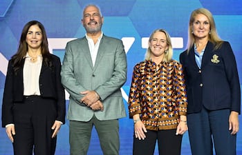 Cuatro personas, dos mujeres y dos hombres, lucen trajes formales en un ambiente festivo, sonriendo cordialmente entre sí.