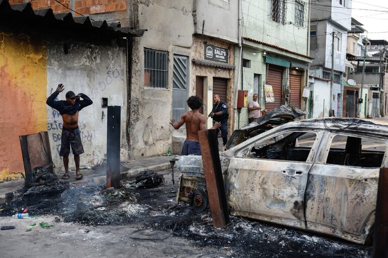 Un integrante de la Policía de Río de Janeiro custodia a dos personas durante un operativo este martes, en Río de Janeiro (Brasil).