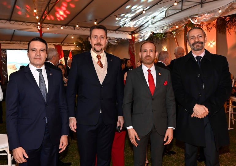 Cuatro hombres en trajes formales, con expresiones tranquilas, dialogando en un entorno decorado con luces suaves.