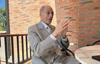 Zaffaroni, hombre mayor con traje claro, sonríe y gesticula con entusiasmo en una terraza con mesa de mármol.