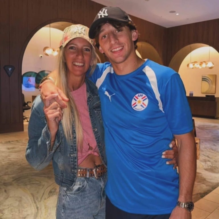 Matías Galarza sonriente con gorra negra y camiseta azul junto a mujer de cabello rubio y abrigo de mezclilla.