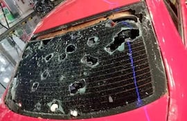 Parabrisas negro de vehículo con múltiples agujeros y fracturas, con reflejos que indican un ambiente exterior húmedo.