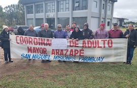 Grupo de adultos mayores de Arazapé sosteniendo un cartel, todos con ropa de abrigo y expresiones de felicidad y tranquilidad.