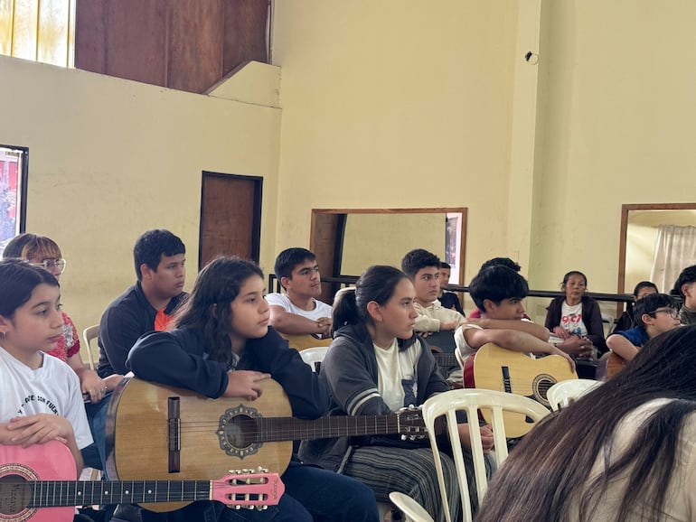 Grupo de seis jóvenes con guitarras, concentrados en un taller musical en un ambiente sencillo y luminoso.