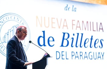 Carlos Carvallo Spalding en traje oscuro y corbata, habla en un podio con un documento en la mano frente a una gran pantalla.
