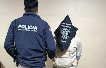 Oficial de policía con chaqueta de investigaciones y sospechoso con capucha negra, en entorno austero y neutral.