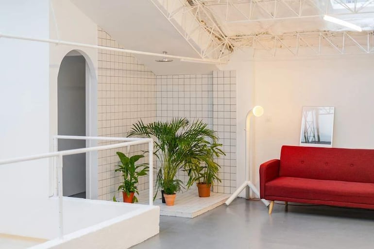 Ambiente minimalista con sillón rojo, planta en maceta y pared de azulejos blancos, sin personas visibles.
