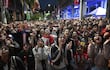 Jóvenes animados con camisetas rojas, blancas y azules, mientras algunos levantan los brazos y gritan en celebración en un ambiente vibrante.