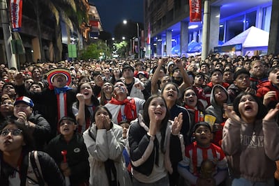 Jóvenes animados con camisetas rojas, blancas y azules, mientras algunos levantan los brazos y gritan en celebración en un ambiente vibrante.