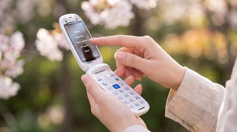Mano sosteniendo un teléfono móvil tipo flip en un entorno natural lleno de flores.