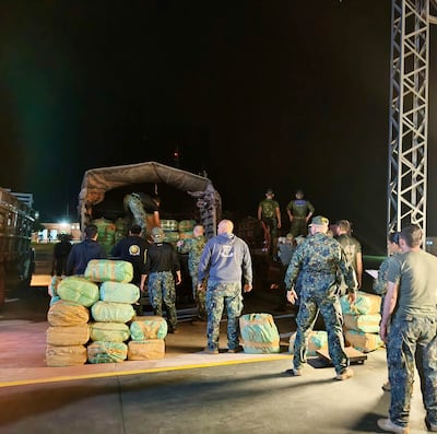Grupo de personas con prendas oscuras organizando paquetes rectangulares en un área iluminada por luces de seguridad.