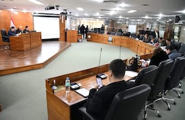 Miguel Sosa sentado con teléfono móvil, rodeado de personas en un ambiente formal, atentos a la discusión.