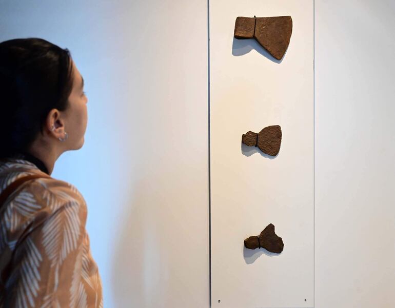 Mujer con camisa de hojas observa herramientas en exhibición en un museo. Ambiente interior, atención concentrada.