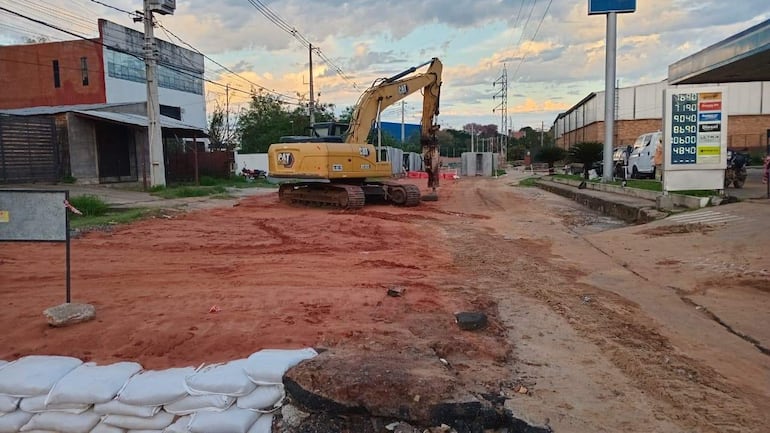 Excavadora Caterpillar trabaja en obra vial, con fondo de sacos apilados y un cielo anaranjado.