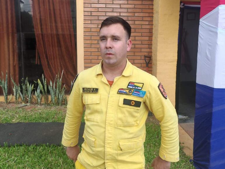 Hombre con uniforme amarillo de emergencia, de pie frente a una pared de ladrillos, con aspecto serio.
