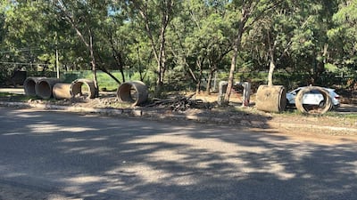 Tuberías de concreto y restos de ramas en la calle de Santo Domingo, con árboles y cerca verde al fondo.