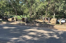 Tuberías de concreto y restos de ramas en la calle de Santo Domingo, con árboles y cerca verde al fondo.
