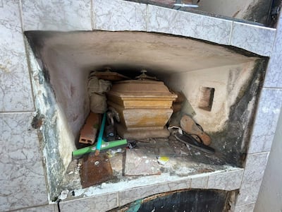 Nicho deteriorado con un ataúd marrón y escombros visibles, reflejando el abandono del cementerio.