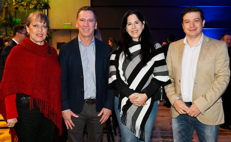 Cuatro personas sonrientes: mujer con abrigo rojo, hombre en blazer oscuro, mujer con poncho a rayas, hombre en blazer claro.