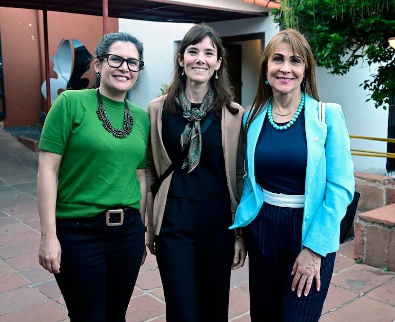 Tres mujeres sonríen en un entorno urbano, con blusas formales: verde, negra y chaqueta azul clara.