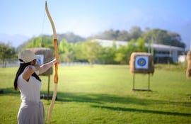Una mujer practica tiro con arco al aire libre, apuntando a dianas de paja.