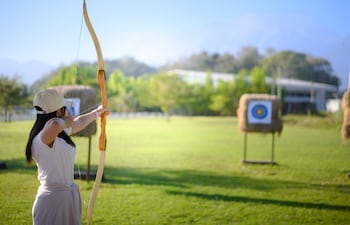 Una mujer practica tiro con arco al aire libre, apuntando a dianas de paja.