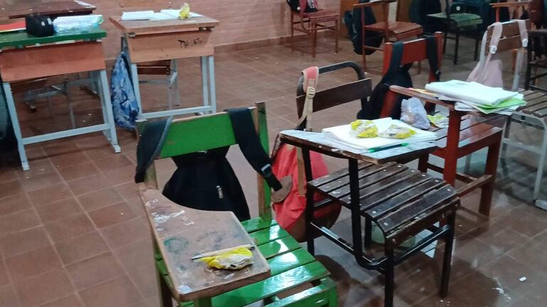 Aula vacía con escritorios de colores y documentos en mesas, revelando uso reciente en la Escuela San Miguel.