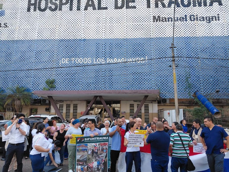 Grupo de personas reunidas con carteles frente al Hospital del Trauma, visiblemente motivados y sosteniendo una bandera nacional.
