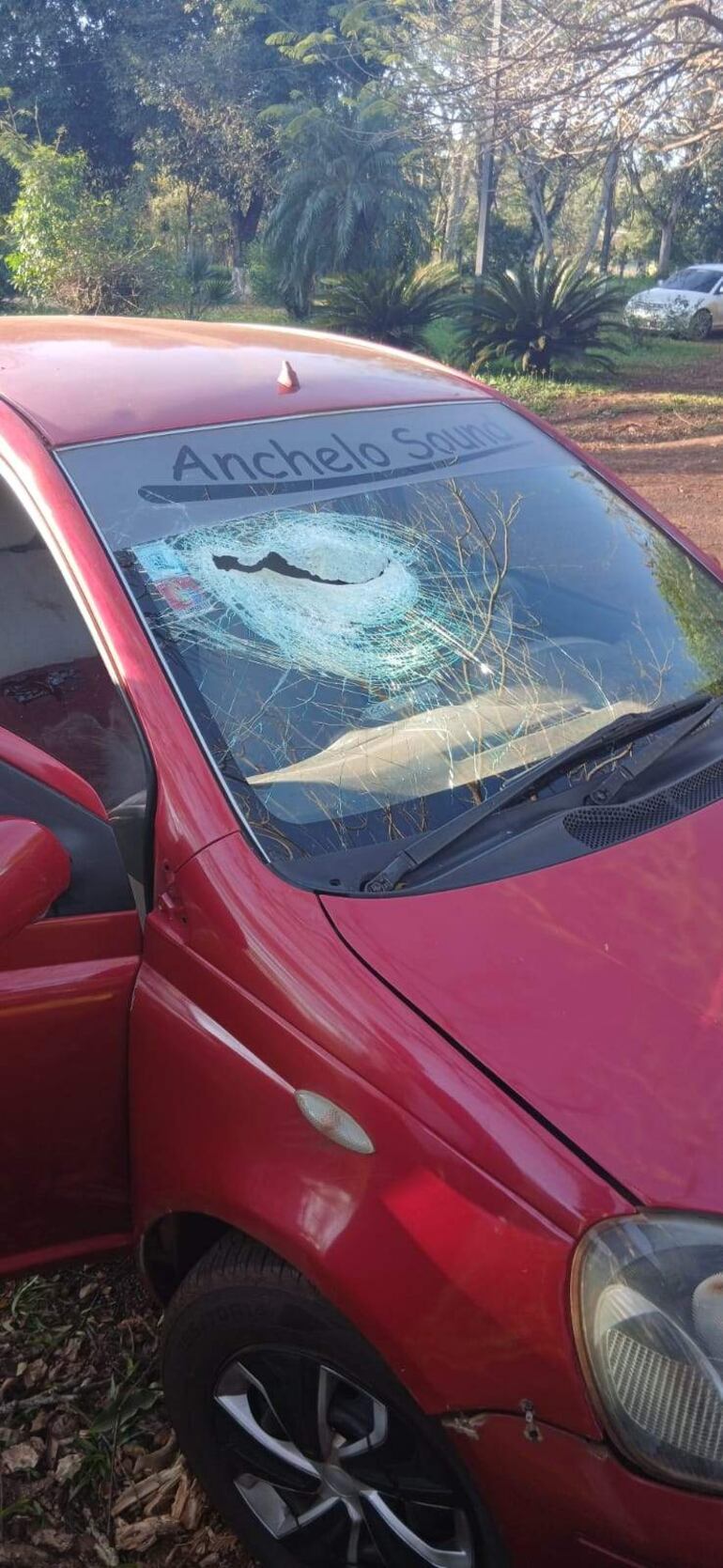 Automóvil rojo con parabrisas destrozado en entorno natural, sin personas visibles ni elementos identificativos.