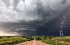 Paisaje natural con cielo gris oscuro y rayo, camino de tierra y colinas verdes al fondo.