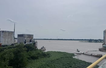 Paisaje natural con río marrón y estructuras industriales para tratamiento de agua, sin presencia humana.