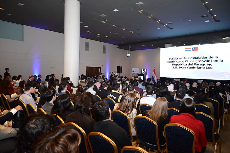 Iván Yueh-jung Lee habla en el escenario ante una multitud de asistentes en ambiente formal y bien iluminado.