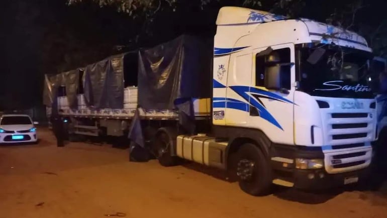 Camión blanco con detalles azules, estacionado en una calle oscura, cubierto con lonas, sin personas visibles.