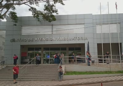 Cinco personas en la entrada del moderno Centro de Atención Ambulatoria, algunas conversan y otras esperan pacientemente.