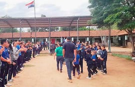 Grupo de niños con camisetas azules y educadores aplaudiendo en un camino central, con bandera paraguaya ondeando al fondo.