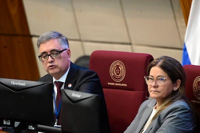 Miguel Báez Reyes, hombre canoso con traje oscuro, habla en el Legislativo. Mujer con chaqueta gris escucha atentamente.