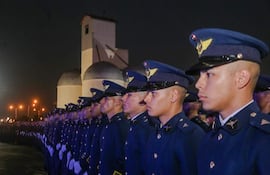 Oficiales en uniformes azules oscuros observan atentamente, en un ambiente solemne y nocturno con luces de fondo.